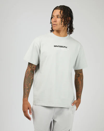 Person wearing a St Goliath light gray t-shirt with a St Goliath brand logo on a white background