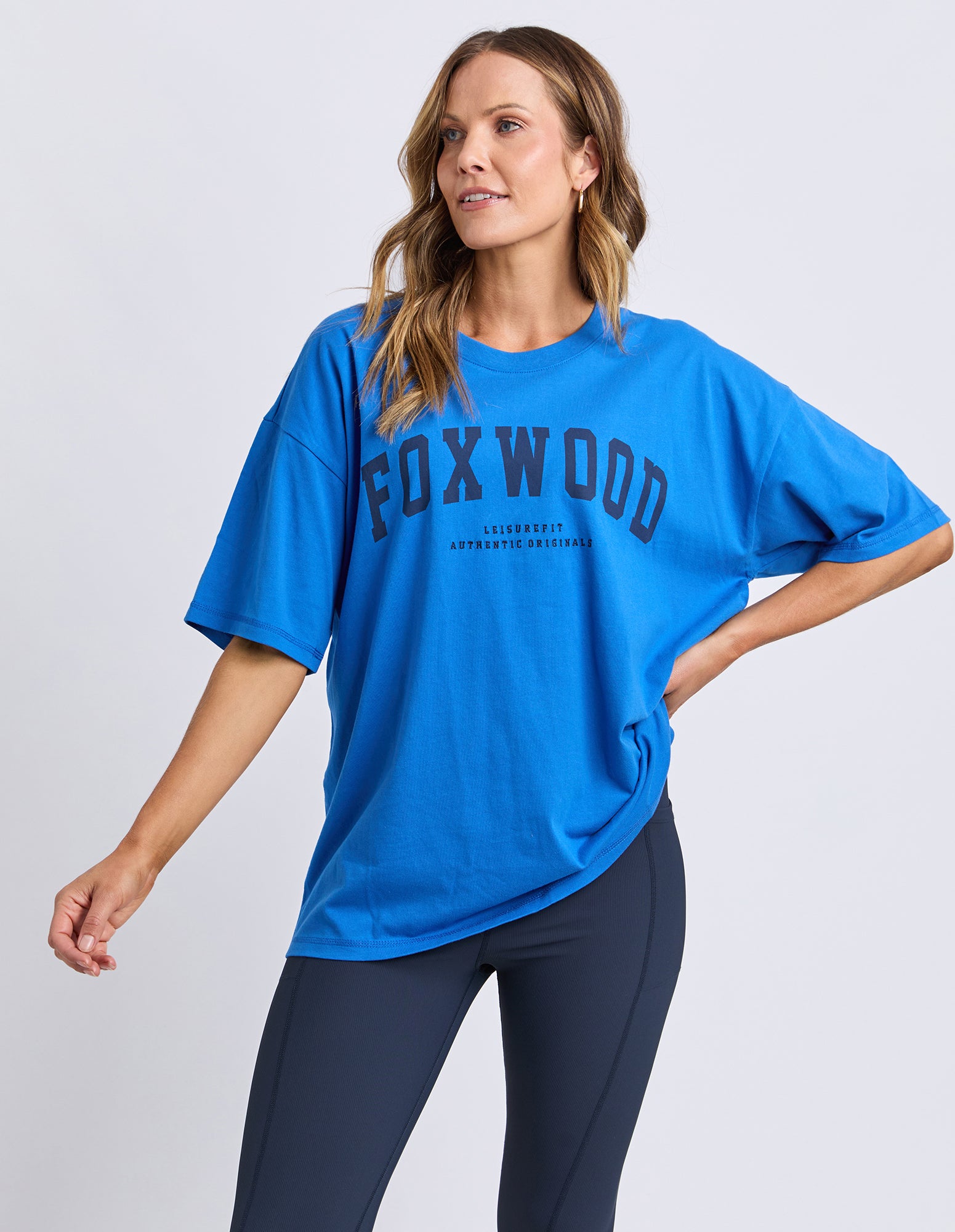 Woman wearing a blue FOXWOOD interval t-shirt on a light gray background