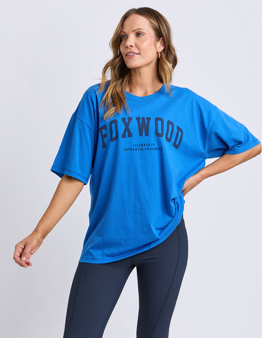 Woman wearing a blue FOXWOOD interval t-shirt on a light gray background