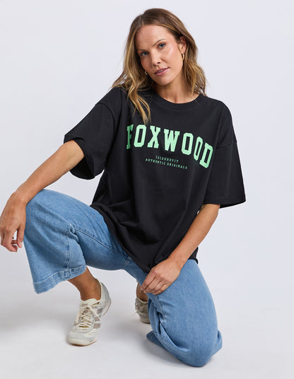 Person wearing a black Foxwood Interval t-shirt with 'FOXWOOD' printed in green on a white background