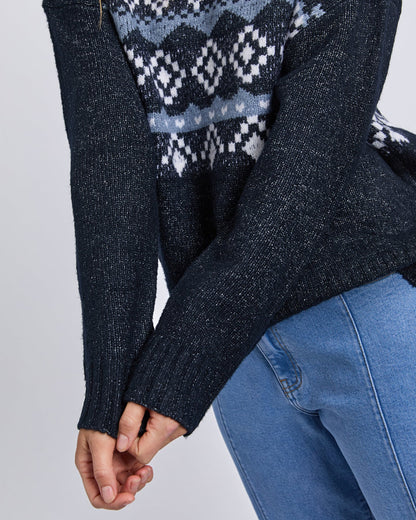 Close‑up of navy knit fabric and warm‑toned intarsia detailing.