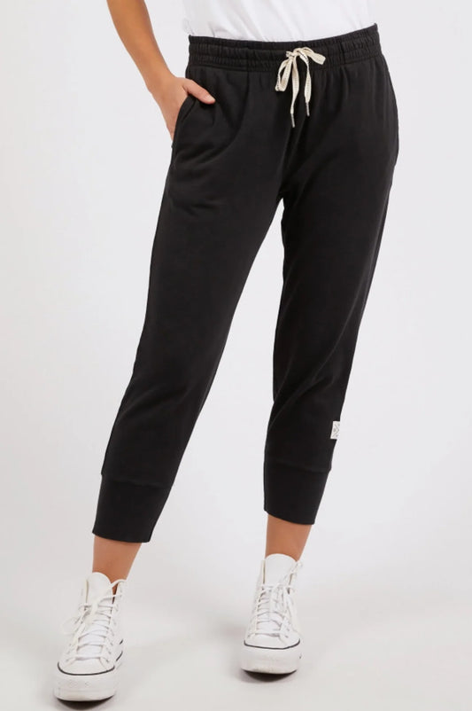 Person wearing ELM Brunch black jogger pants with a white logo on a white background